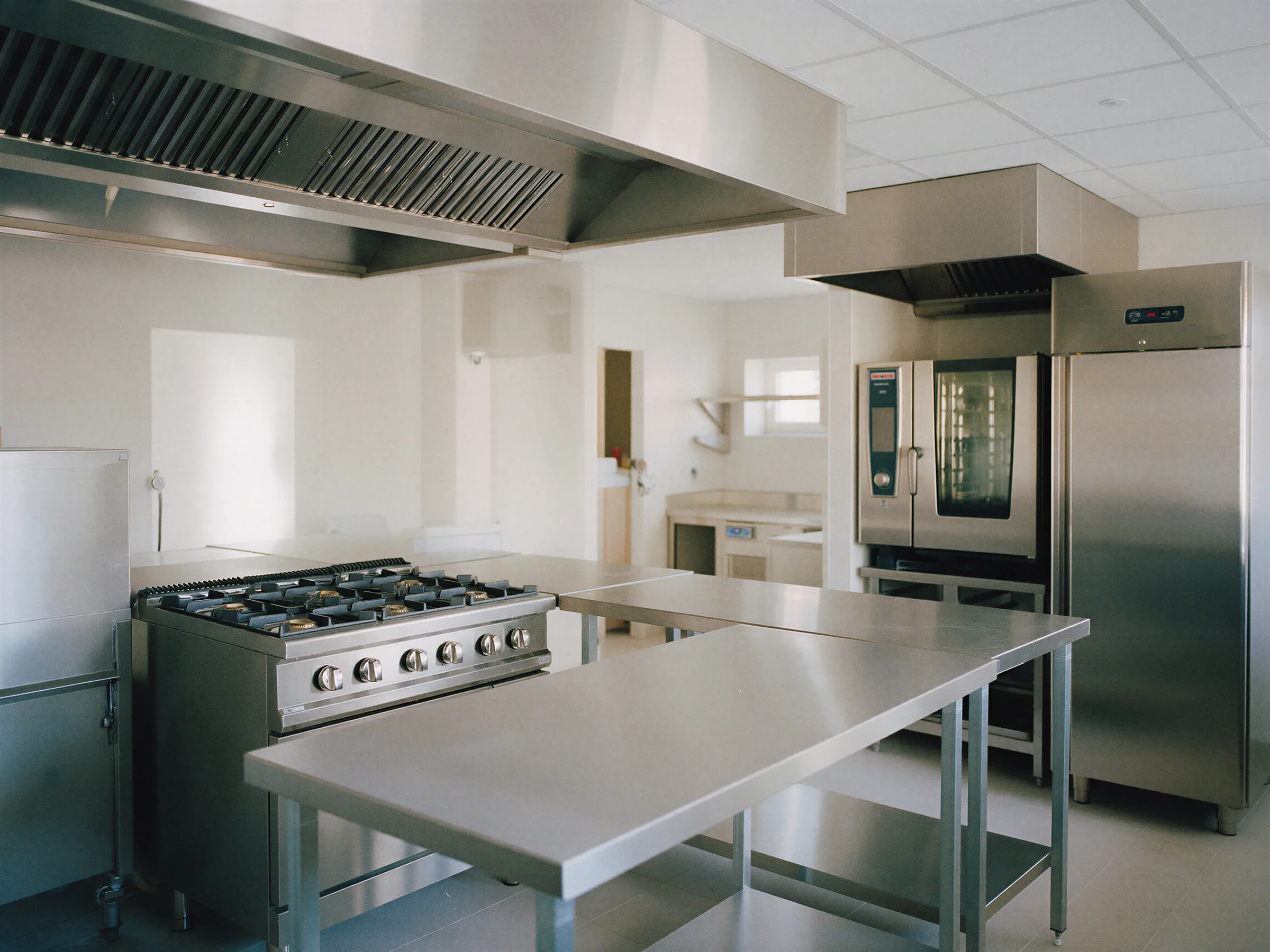 Cocina profesional recién instalada con cocina de fuegos, campana, mesas de acero y horno