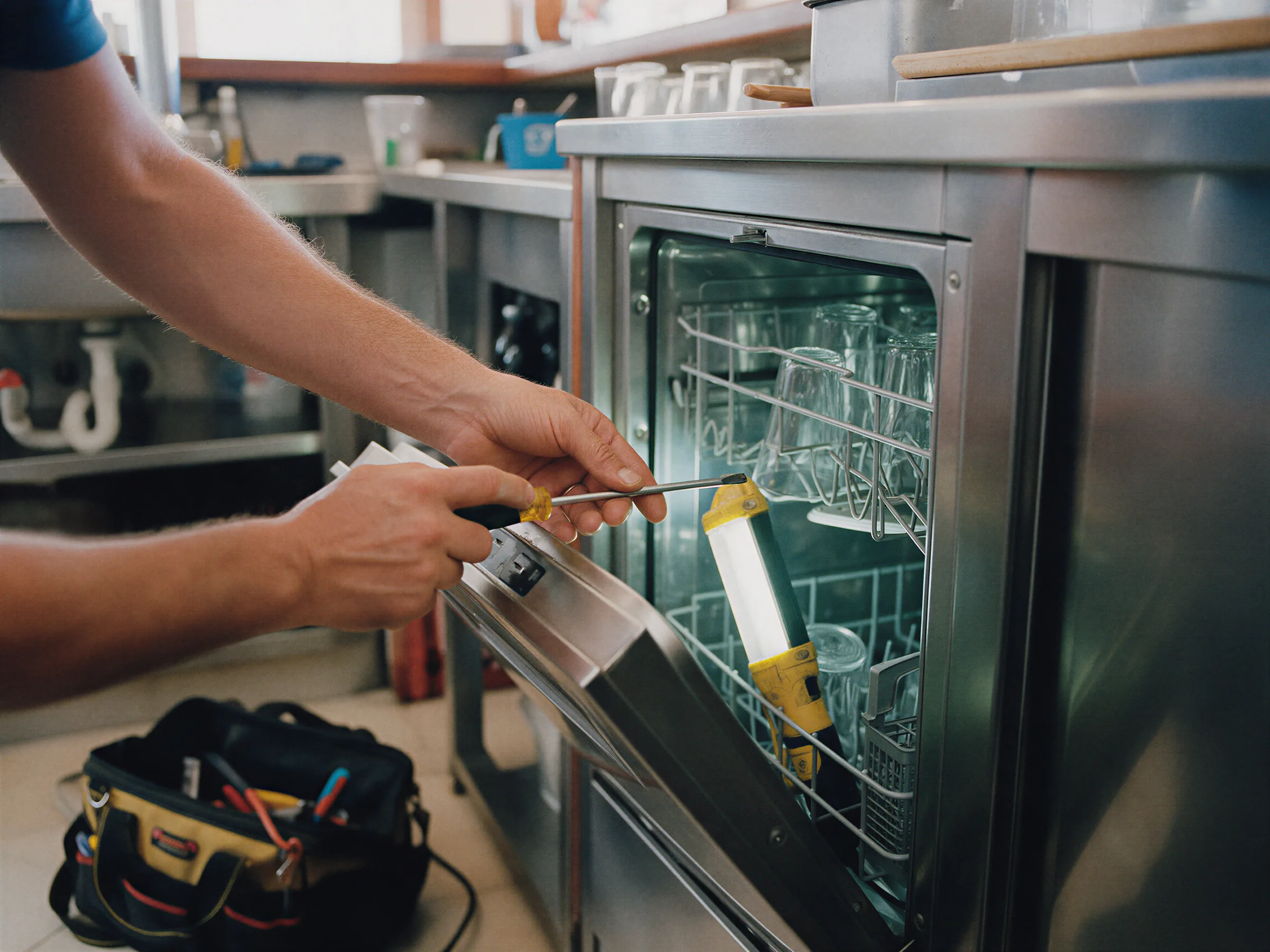 Técnico revisando el panel de un lavavasos de acero bajo una barra