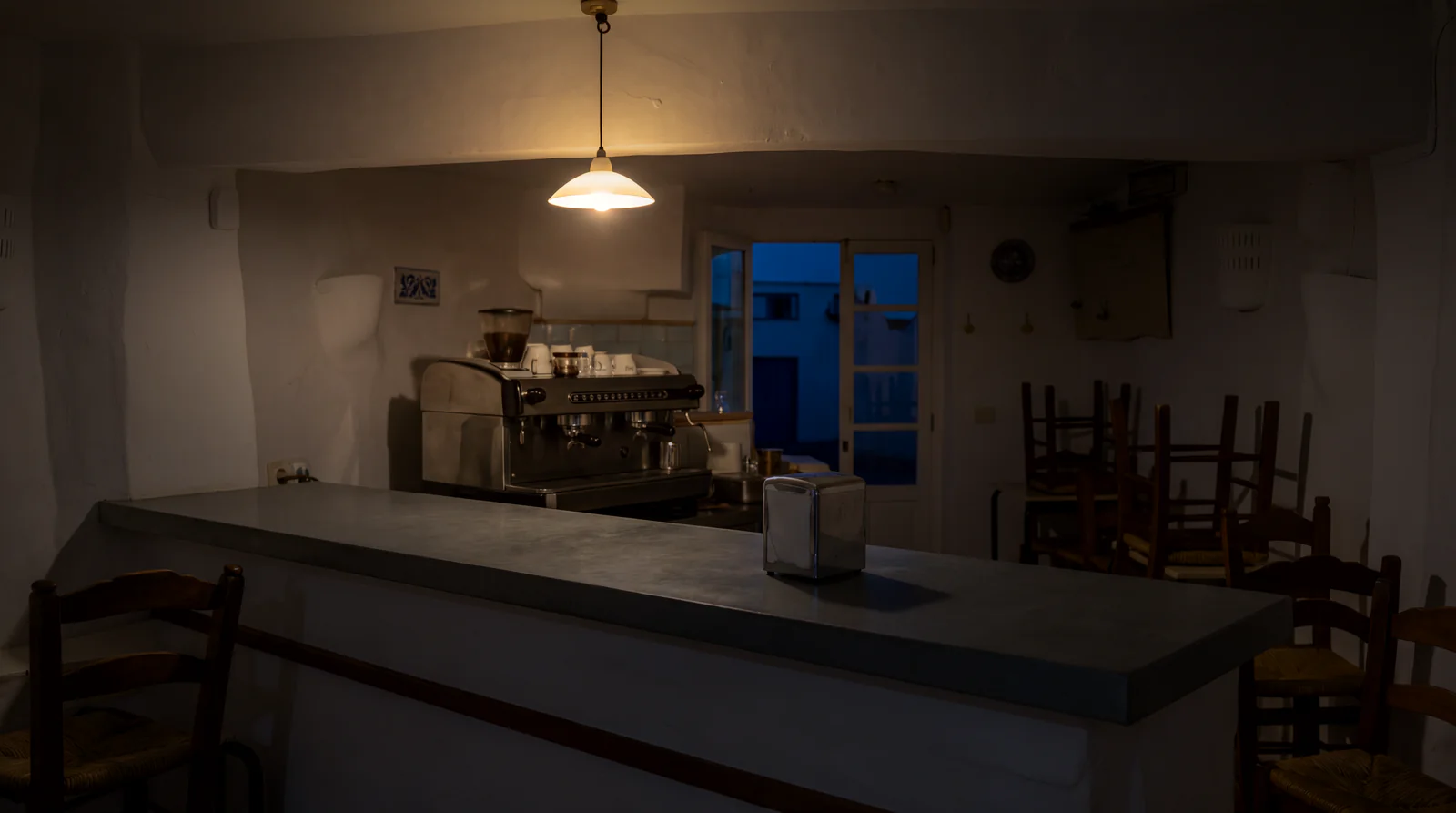 Interior de un bar cerrado de noche, con las sillas sobre las mesas y una lámpara encendida sobre la barra